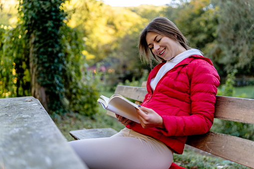 Amidst nature's beauty, a young woman discovers an escape into literature on a bench, where the rustling leaves and gentle breeze accompany her literary journey
