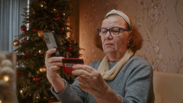 Attractive mature woman sitting in front of computer and entering details of bank card stock photo