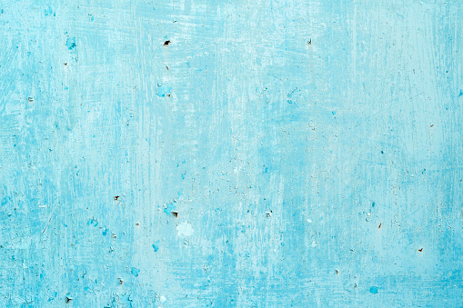 A close-up of a weathered plastered concrete wall painted in blue, showcasing the textured and aged surface.