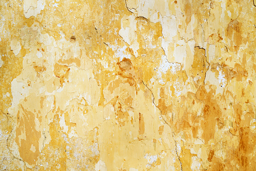 Flaking yellow white paint on the stucco exterior wall of an old house building