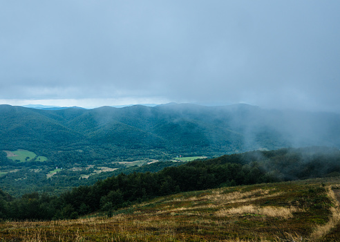 Beautiful scenery of grass fields covering a side of a hill or a mountain with mountain range in the distance