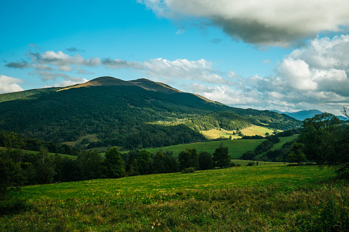 Beautiful scenery of grass fields covering a side of a hill or a mountain with mountain range in the distance