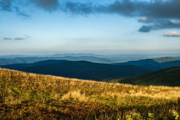 Beautiful scenery of grass fields covering a side of a hill or a mountain with mountain range in the distance