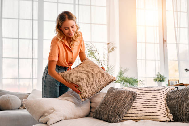 Beautiful lady with wavy blond hair adjusting soft cushions on modern sofa.