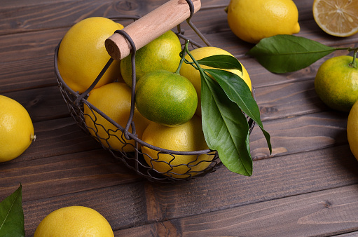 Ripe citrus fruits with leaves in a metal basket on a dark wooden background. Selective focus.