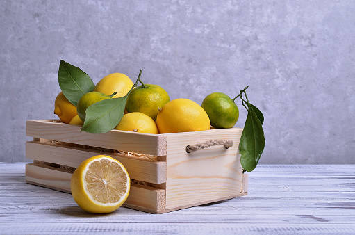 Ripe citrus fruits with leaves in a wooden box on a light wooden background. Selective focus.