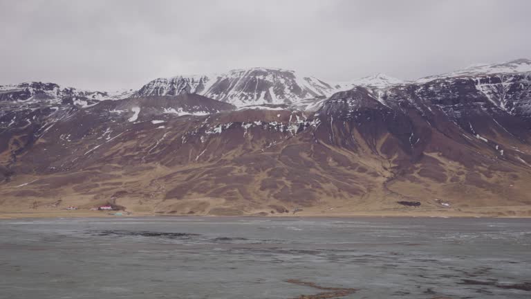 Slow zoom in of Iceland volcanic mountain range landscape near wet meadow