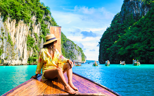 Asian women in front of a longtail boat at Kho Phi Phi Thailand, women in front of a boat at Pileh Lagoon with turqouse colored ocean during a boat trip to Maya Bay Koh Phi Phi