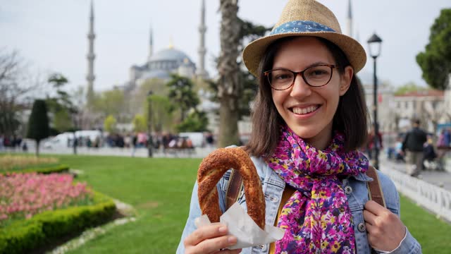 Young Woman Eating A Turkish Bagel In Front Of Blue Mosque In Istanbul