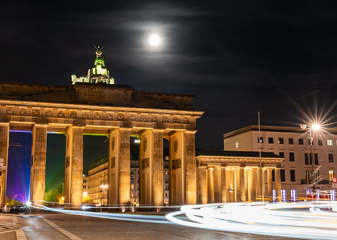 The Brandenburg Gate in Berlin at night, showing the moon in the background and lights of traffic in the foreground
