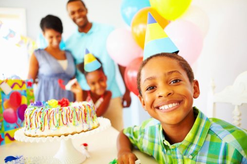 Portrait of a smiling young boy next to birthday cake with his family in background