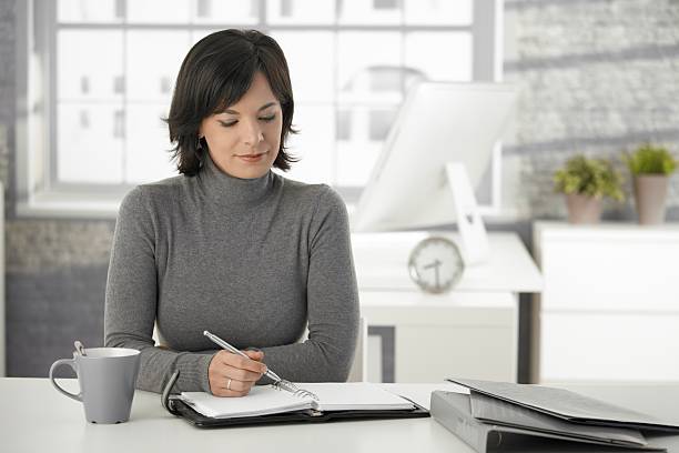 istock Young woman sat at a white desk holding a pen on a notebook 183506658