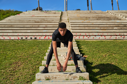 Full body of focused Hispanic male in sportswear looking away and leaning forward while stretching on steps before training on street