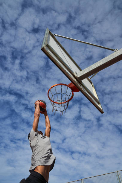 istock Basketball player throwing ball into hoop against cloudy sky 1835072553