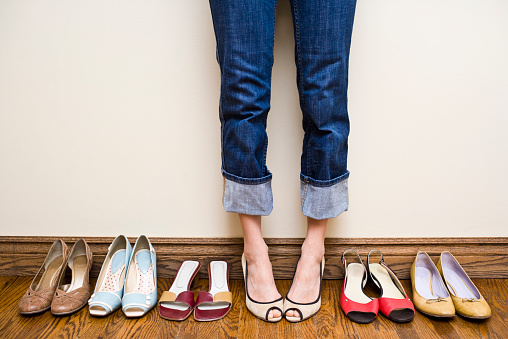 Woman stands in a pair of open toe heels in the middle of a row of shoes showing the concepts of consumerism, individuality, shoe addiction, fashion and shopping