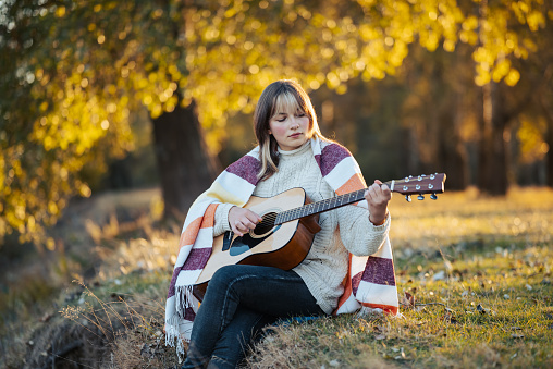 Beautiful girl enjoying fall nature, playing the guitar alone in autumn park