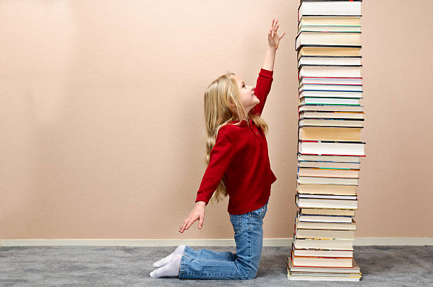 The girl lies on the floor and hugs a yellow book. There are open books around her head. The girl is dreaming. She read a lot.