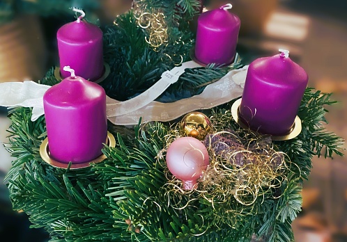 Colorful advent wreath with four white burning candles on wooden background.