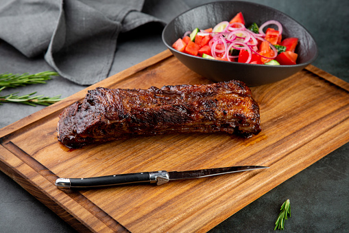 well-done steak with tomato and cucumber salad on a wooden tray, top view