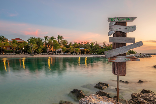 A worn and weathered, wooden signpost, on the shore of a Caribbean beach at sunset