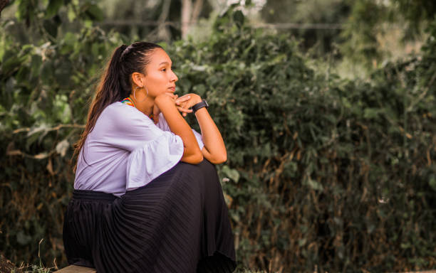 young woman sitting outdoors while wearing calm clothes and hands next to her face