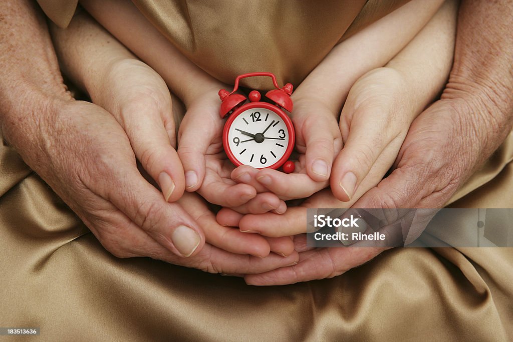 Time for Family "Three generations of hands (grandmother, mother and child) holding a small red clock." Clock Stock Photo