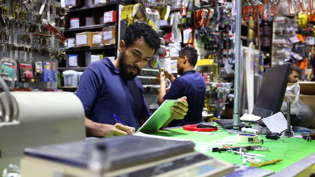 Latin American salesman crosschecking an inventory on a document and tablet at a hardware store