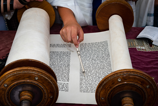 A man reading from the Torah  uses a pointer or yad to guide him through the Hebrew text.
