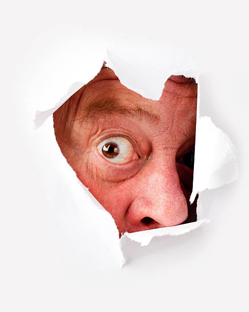 istock Man with funny face staring from hole on white paper 183515282