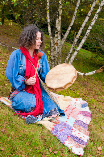 Metis woman outdoors beating a drum while chanting.