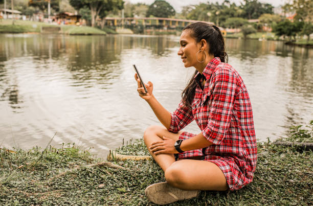istock young woman using her mobile phone while standing on the shore of a lake 1835161029