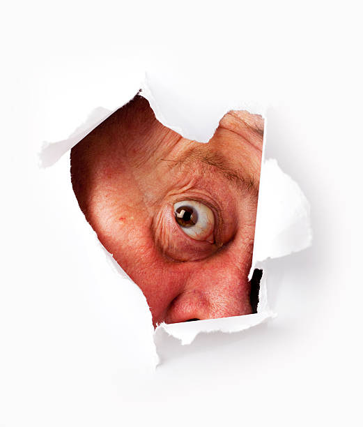 istock Man with funny face staring from hole on white paper 183521963
