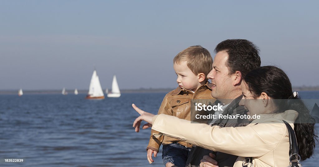 Young family standing at lake Young family standing at waterA's edge. Mother pointing at sailboat. Shallow DOF with selective focus on boy.Please also have a look at my private lightbox: Family Stock Photo