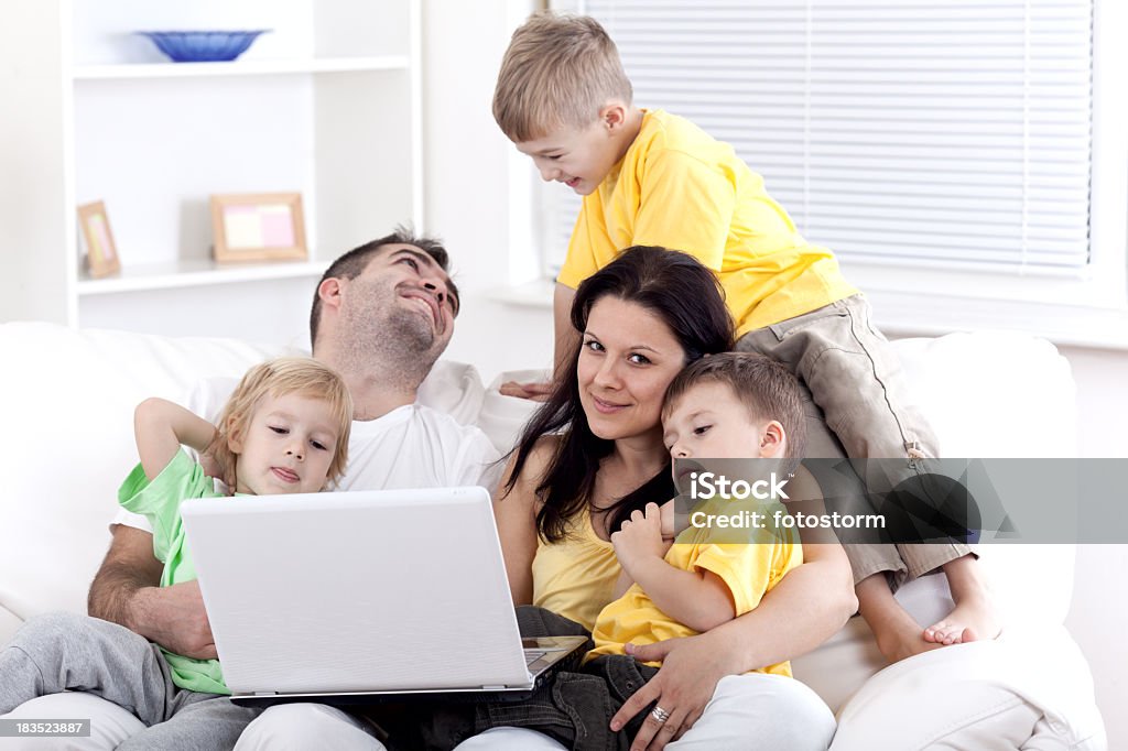 Familia feliz sentado en un sofá en la sala de estar, con capacidad para una computadora portátil - Foto de stock de 30-39 años libre de derechos