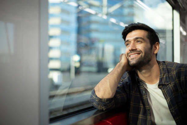 Handsome man is in a public transport train sitting and looking through the window