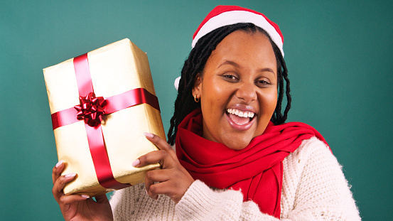 Beautiful Black woman shakes Christmas gift, guess present inside, studio. High quality photo
