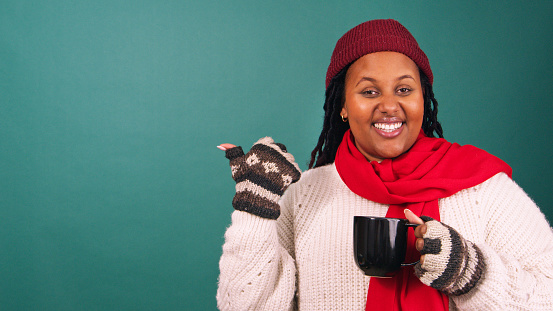 Beautiful young woman in winter outfit points to copy space, Christmas studio. High quality photo