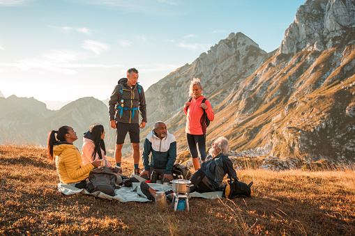 A diverse group of friends takes a scenic tea stop at the picturesque hilltop, backpacks in tow.