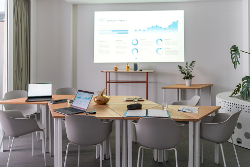In this contemporary corporate environment, laptops and wireless technology are prevalent. A projector showcases statistics on an empty white wall.