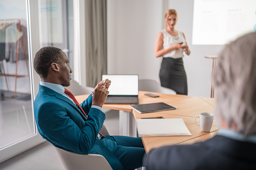 A cluster of multiracial professionals, distinguished by their attractive appearance, discussing and deliberating on business strategies in a corporate setting. Utilizing laptops and wireless technology in a meeting, they present a formal business demeanor.