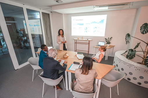 Colleagues of mixed race gathered in a corporate office for discussions on business decisions. Utilizing laptops and wireless technology in a meeting, they actively contribute to a conversation centered around strategic planning.