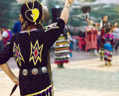 This Powwow was celebrated in White Rock, British Columbia, Canada on 11 March 2018. The Squamish Nation's annual powwow is a gathering of First Nations communities to honour their culture, share, respect, dance and drum. Their heritage is respected by all ages. This image displays a jingle dancer in the foreground and soft focus jingle dancers in the background.