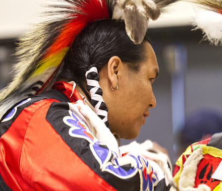 This Powwow was celebrated in White Rock, British Columbia, Canada on 10 March 2018. The Squamish Nation's annual powwow is a gathering of First Nations communities to honour their culture, share, respect, dance and drum. Their heritage is respected by all ages. This is a soft focus profile of a dancer wearing colourful regalia and long braided hair.