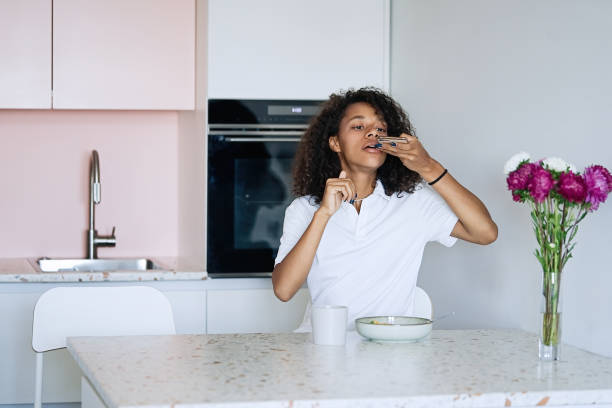 istock Woman sitting at kitchen counter having breakfast and typing a text message using smart phone 1835292684