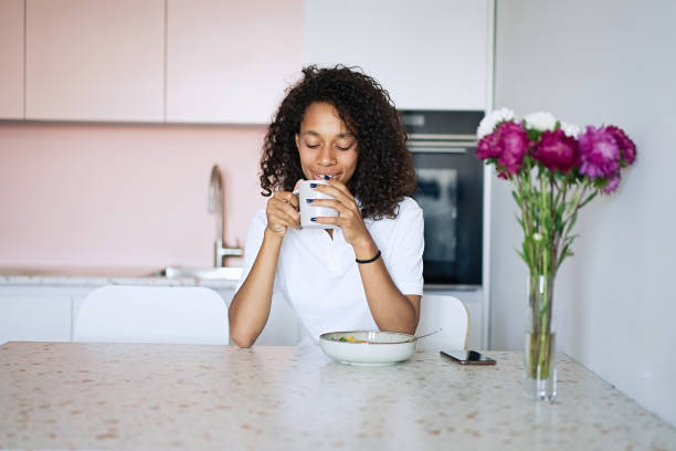 istock Woman sitting at kitchen counter having breakfast and typing a text message using smart phone 1835293213