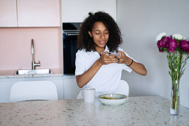 istock Woman sitting at kitchen counter having breakfast and typing a text message using smart phone 1835293250