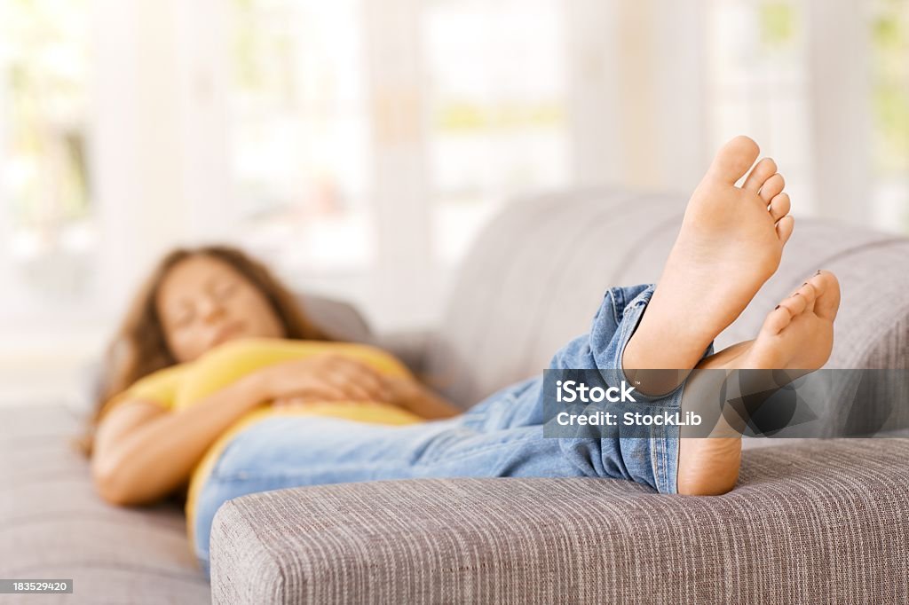 Giovane donna sdraiata sul divano in soggiorno, notte - Foto stock royalty-free di Piedi alzati