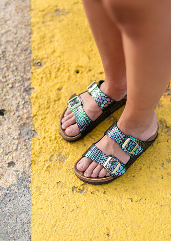 A woman stands on a yellow-painted section of pavement wearing colourful sandals