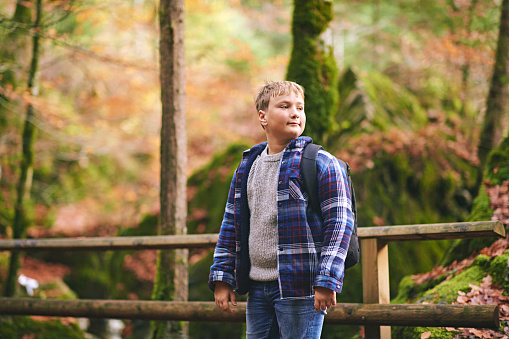 Outdoor portrait of happy kid boy hiking in autumn forest, wearing backpack