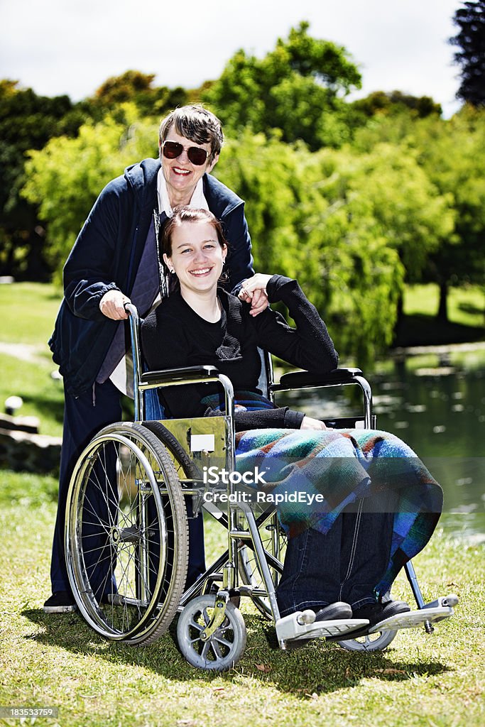 Teenager-Mädchen im Rollstuhl mit älteren Pflegekraft halten Hände, Lächeln - Lizenzfrei 60-69 Jahre Stock-Foto